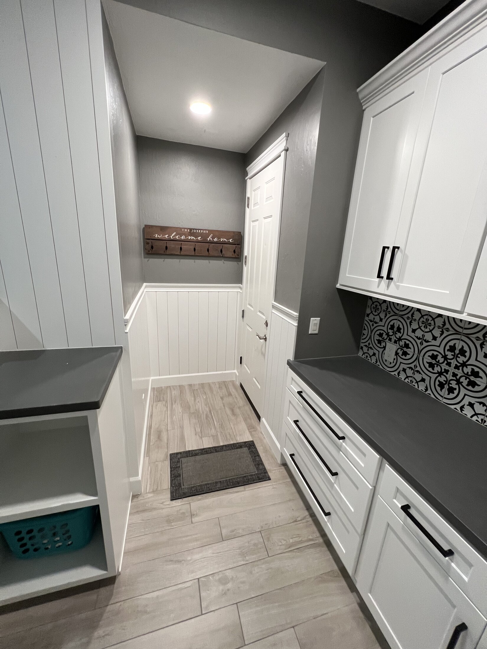 Remodeled laundry and mudroom with white shaker cabinetry, gray quartz counters, patterned tile backsplash, and shiplap wainscoting