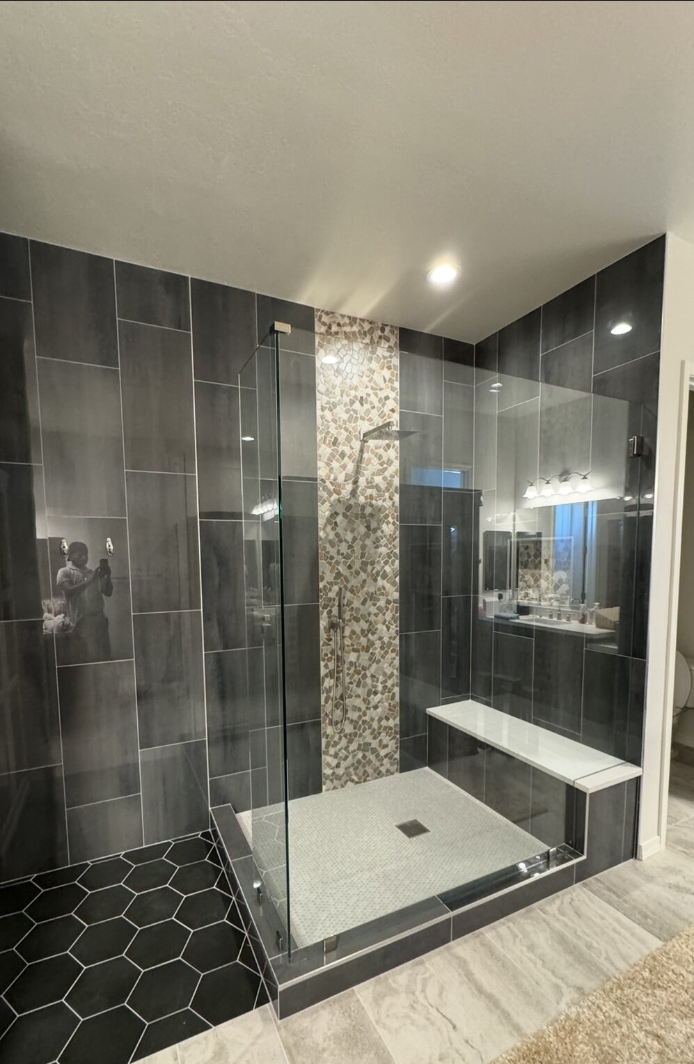 Custom walk-in shower with floor-to-ceiling dark tile, bench seat, and hexagon tile floor after JBS remodel
