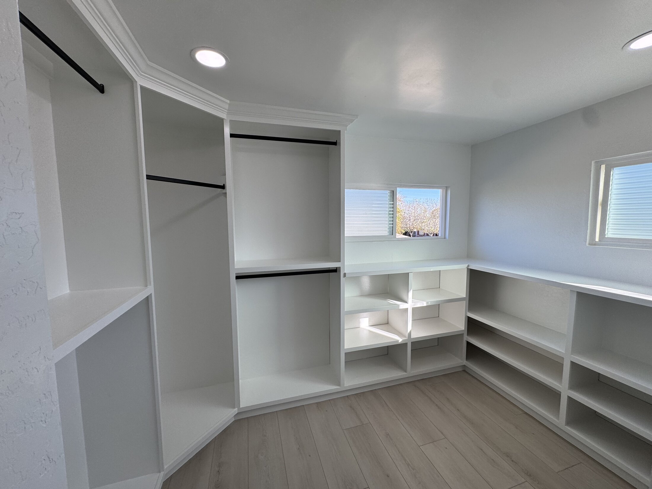 Custom walk-in closet with wall-to-wall white built-in shelving, hanging rods, and shoe cubbies