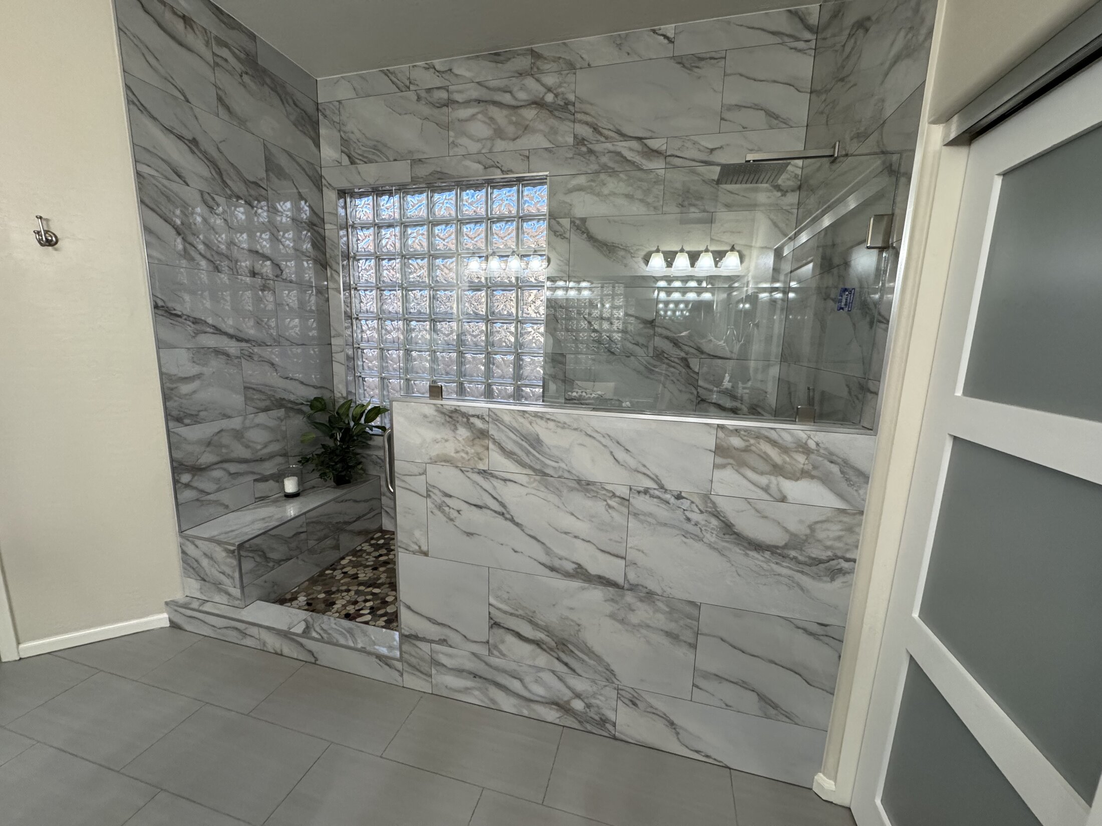 Marble-tiled master bath walk-in shower with glass block window, frameless glass panel, and built-in tile bench